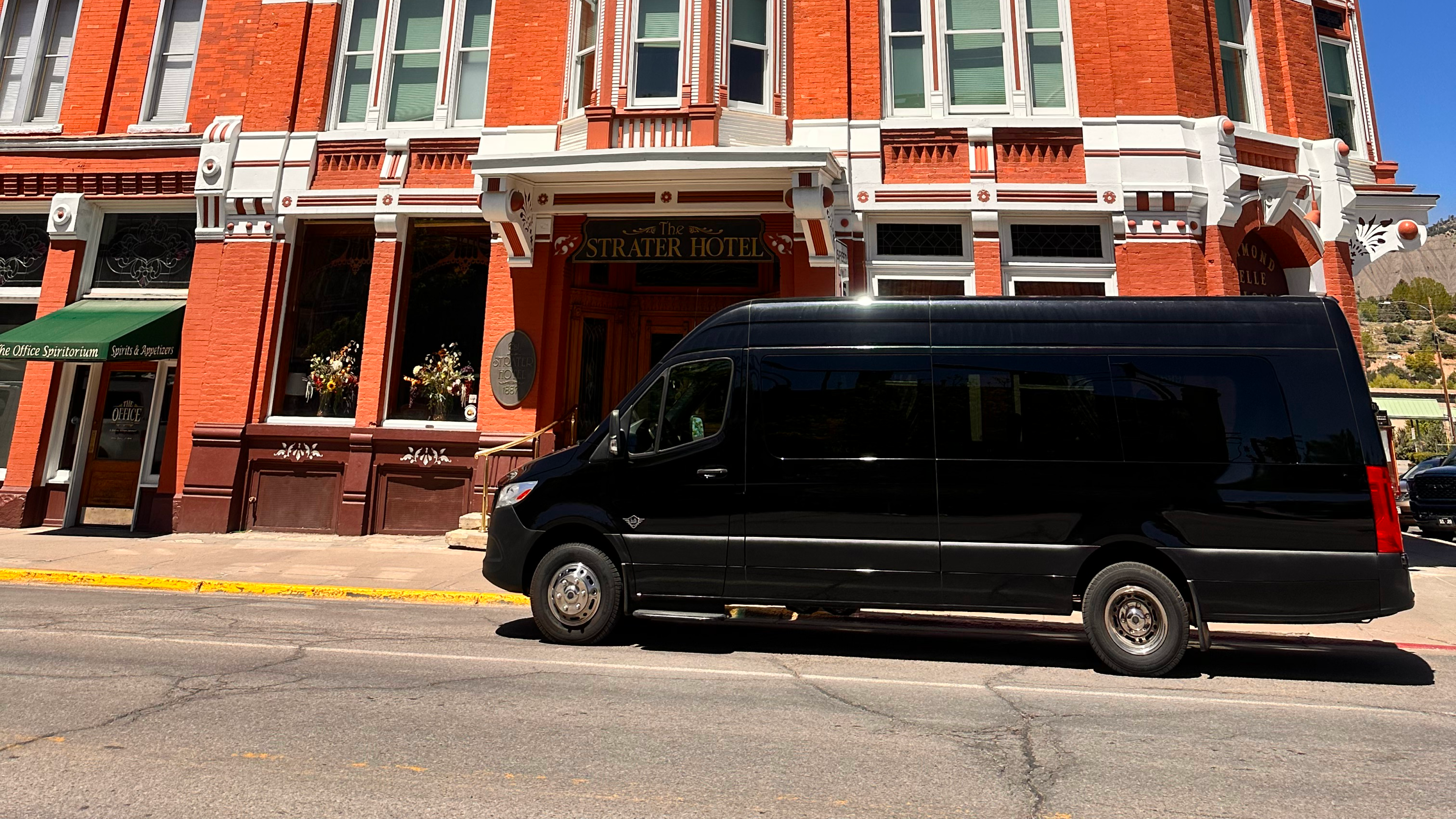 Black Mercedes Sprinter van parked in front of the historic Strater Hotel on a sunny day, highlighting its luxury and suitability for upscale locations.