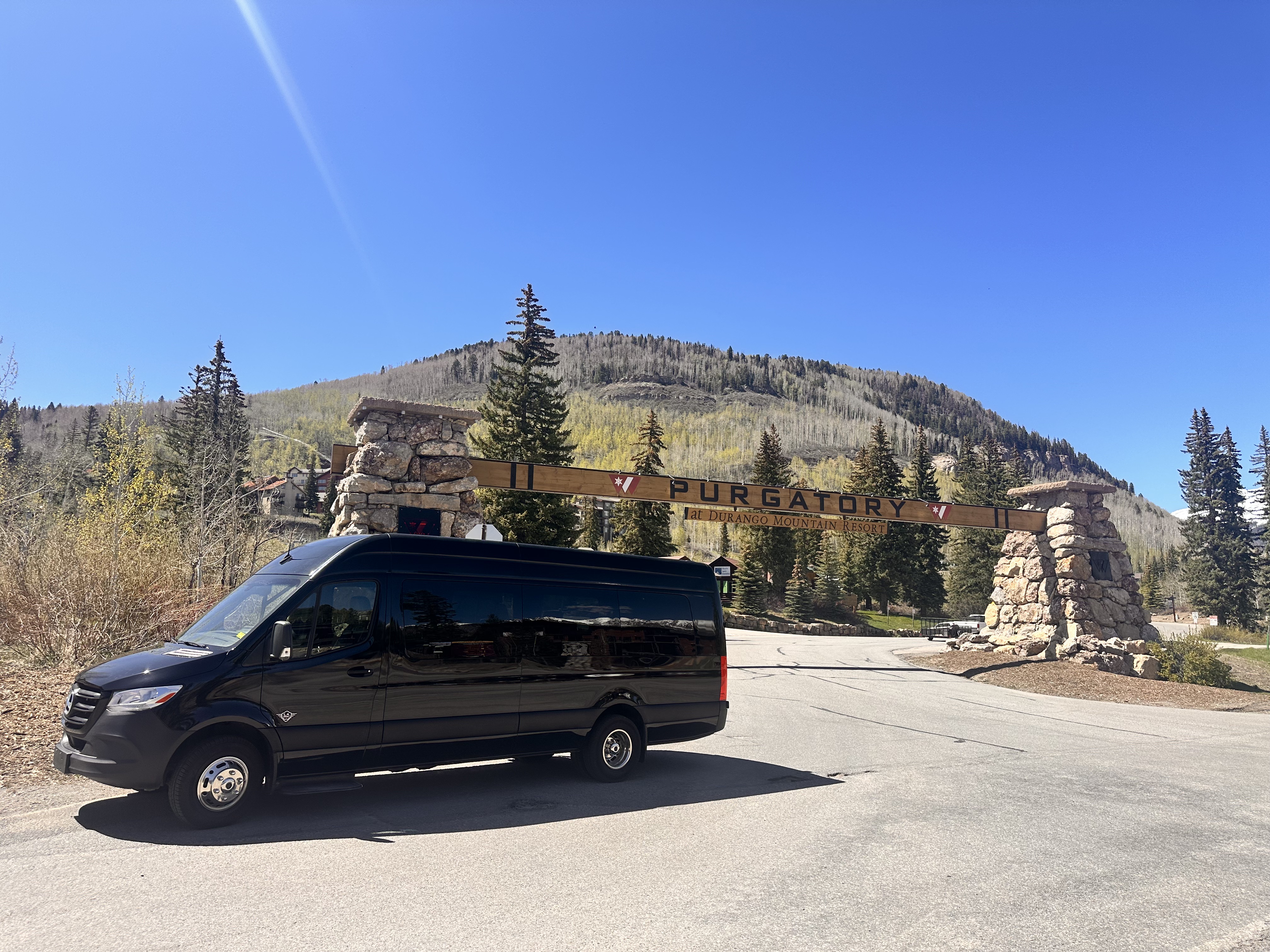 Black Mercedes Sprinter van positioned at the Purgatory at Durango Mountain Resort entrance sign, with majestic mountains in the background, ready for adventure.