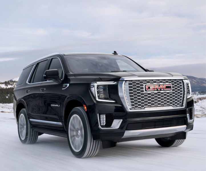Detailed interior shot of a GMC Yukon Denali, focusing on the plush brown leather seats, wood grain accents, and the modern dashboard layout.